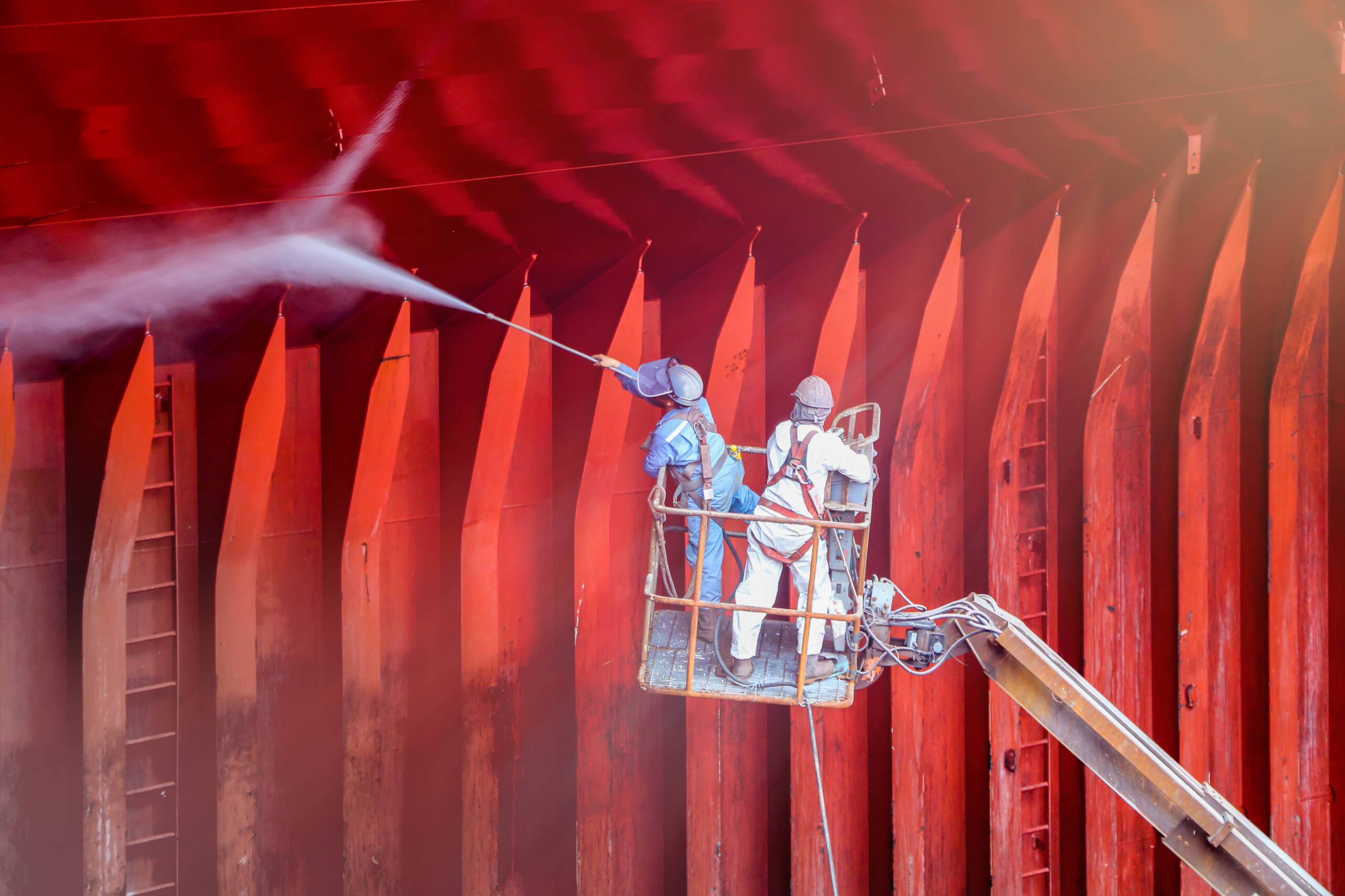 two workers perform cargo hold cleaning with high pressure washer